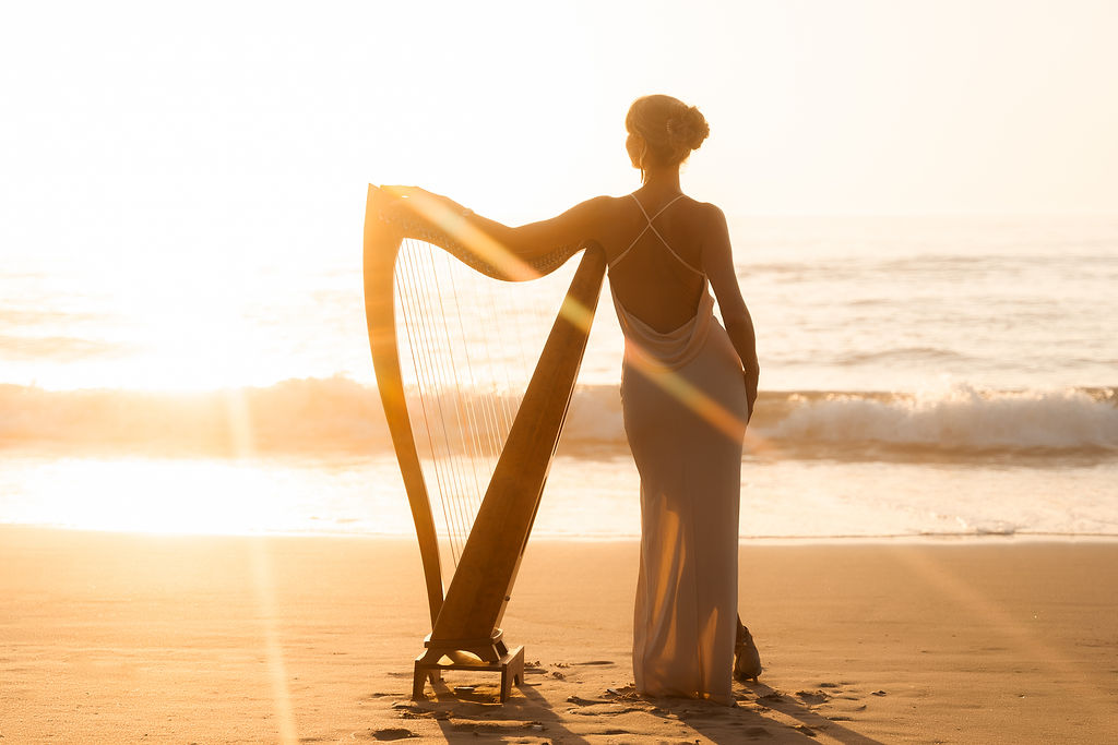 Danielle Riegel standing with her harp by the ocean at sunset