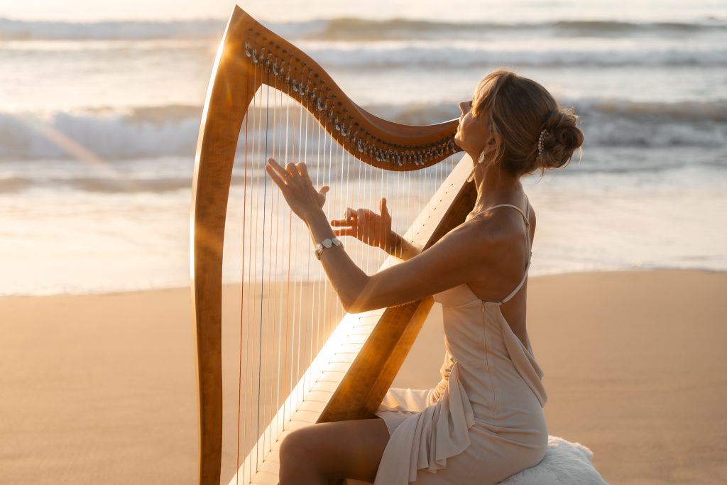 Danielle Riegel playing her harp on the beach by the ocean