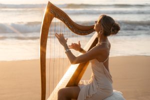 Danielle Riegel playing her harp on the beach by the ocean