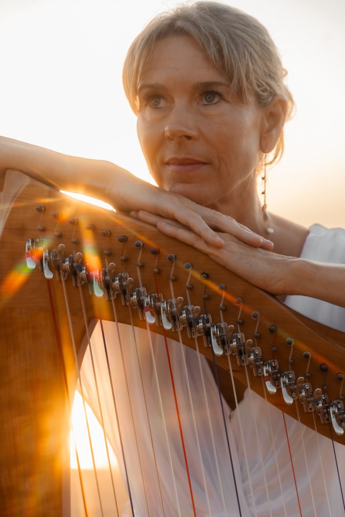Close-up portrait of Danielle Riegel resting her hands on her harp at sunset