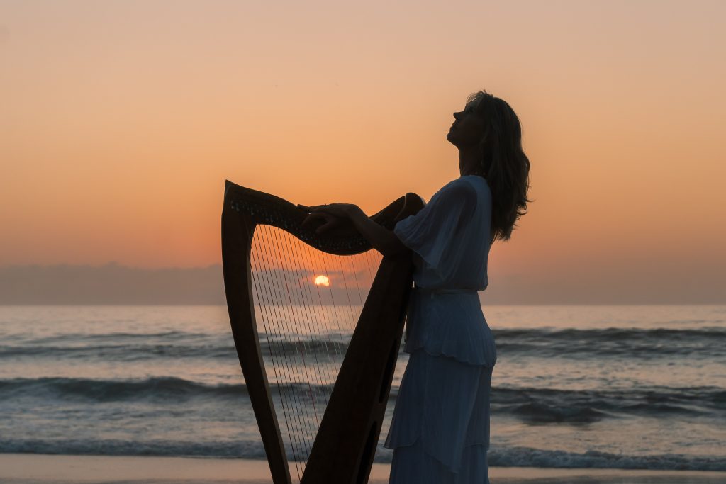 Danielle Riegel standing with her harp on the beach at sunset