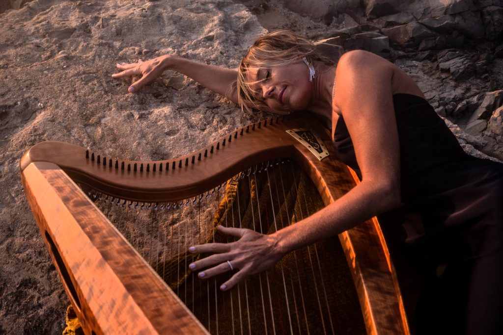 Danielle Riegel resting against her harp on coastal rocks